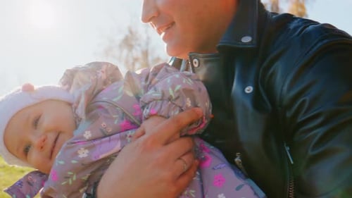 Affectionate father holds baby girl outside in sunlight