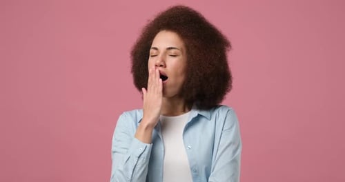 Joven mujer afroamericana bostezando, cubriéndose la boca con la mano, cansada, sintiéndose somnolienta, fatigada y aburrida