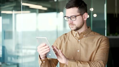 Close up. Confident businessman in shirt is using tablet while standing in business office.