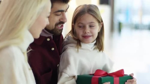 Closeup of Happy Young Parents Giving Gifts to Loving Little Daughter in Shopping Mall Spending