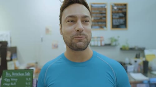 Cheerful Man in 30s Eating Fresh Salad Smiling Looking at Camera Inside Small Cafe