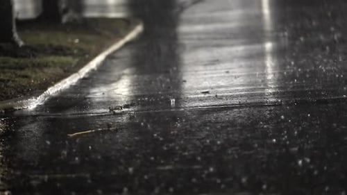 Regen fällt nachts auf reflektierende Stadtoberfläche, keine Menschen