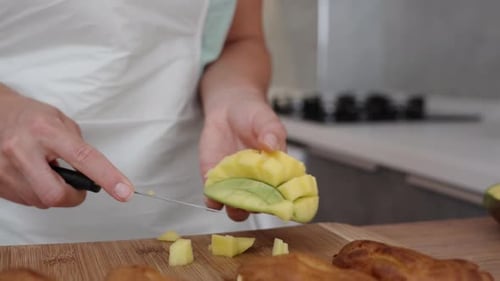 Die Frau schneidet Mangowürfel auf einem Holztisch.