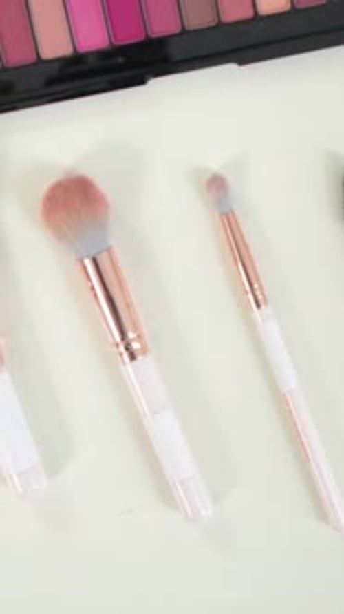 Vertical video: Panning camera revealing brushes, palette and lipstick on pale table for display