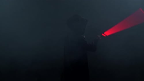 Young Man in Jedi Cosplay Costume with Lightsaber Battle on Black Background in Smoke and Rain Slow