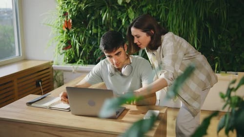 Dans un espace de travail moderne, de jeunes professionnels collaborent sur un ordinateur portable entouré de verdure pour promouvoir