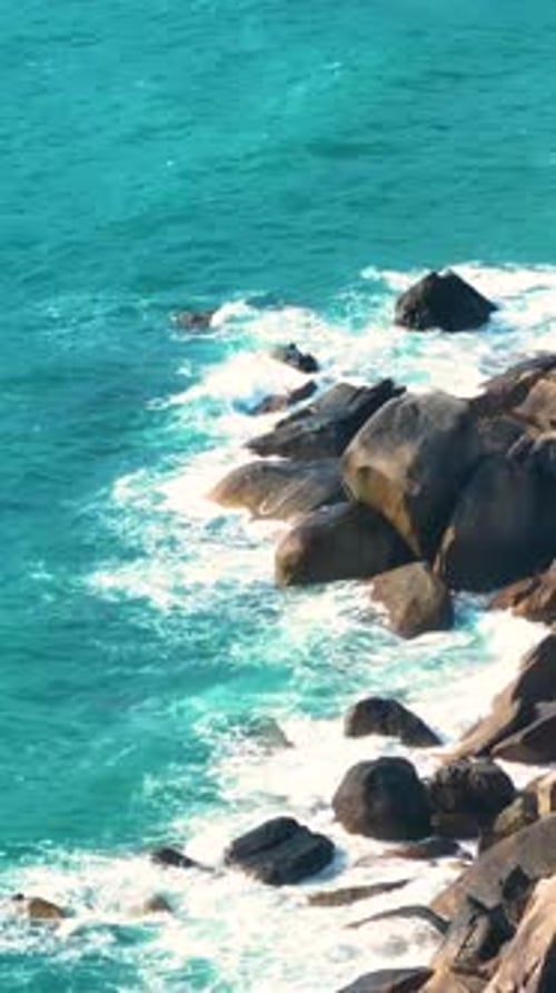 Les vagues s'écrasent sur les rochers escarpés au bord d'un océan turquoise sous un soleil éclatant. Verticale