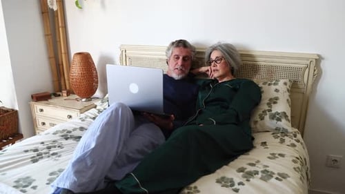 Senior couple using laptop while relaxing in bed