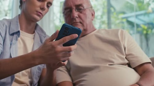 Young Man Helping Senior Man Use Smartphone