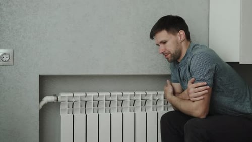 Caucasian Man Sits Near Heating Radiator and Tries to Warm Up