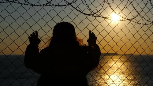 Refugee Child Looking at Sunset Through Barbed Wire Fence