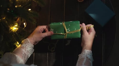 Woman Wraps Holiday Gift with Gold Ribbon