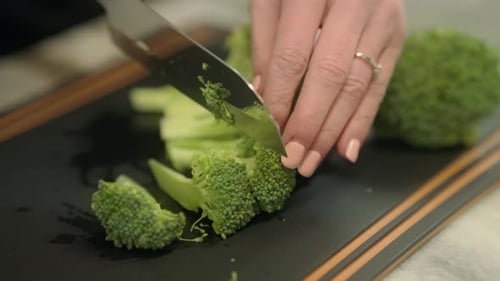 Stems of broccoli are slices through with a knife on a cutting board.