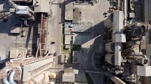 Drone footage of heavy industry cement factory with silos, conveyors, and chimneys in operation