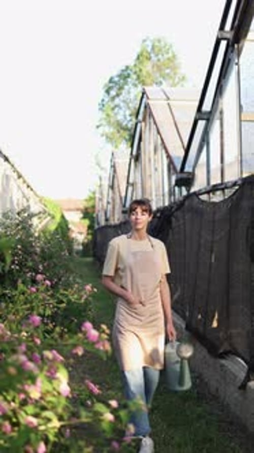 Gardener Walking Along Greenhouses Carrying Watering Can