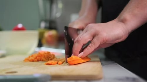 Close-up of hands cutting carrot with large knife on wooden board