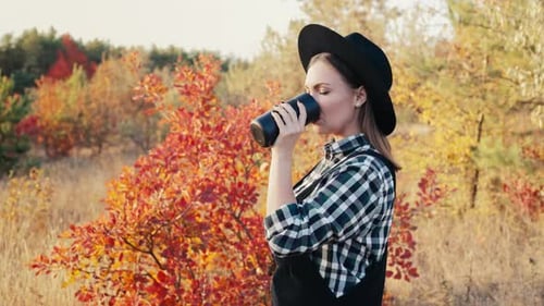 Hipster Woman Drinking Hot Coffee or Tea Thermos Golden Park Forest in Autumn