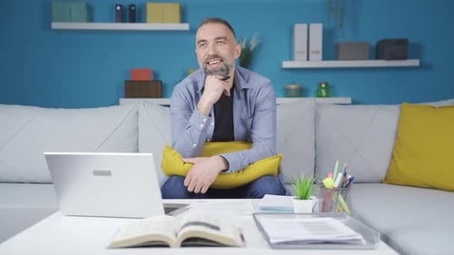 Man Thinking with Laptop and Book at Home