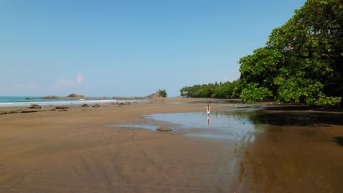 Woman in white dress walks alone on wide tropical beach in sunny Costa Rica