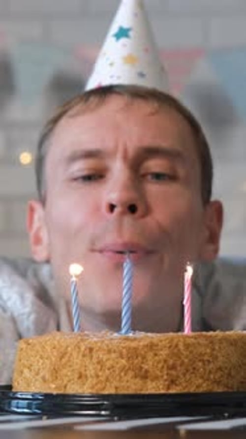 Man in Party Hat Blows Out Birthday Candles
