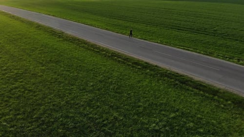 Woman Running on Road Through Green Field