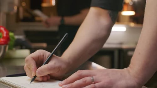 Chef Writing Menu Notes and Talking to Colleague in Restaurant Kitchen