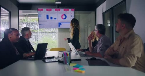 Businesswoman explains data chart to engaged team during office presentation while group