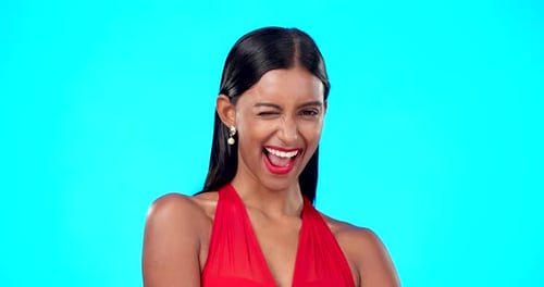 Wink, happy woman face and studio with isolated blue background and a flirty model