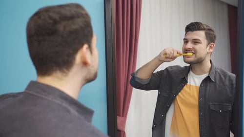 Young Adult Brushing Teeth in Bathroom Mirror