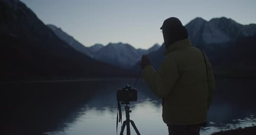 Photographer with Camera on Tripod By Mountain Lake at Dusk
