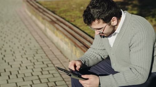 Jeune homme d'affaires utilisant une tablette sur un banc en ville