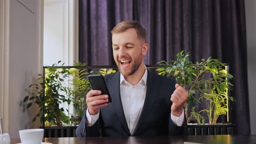 Man Celebrates Success While Using Smartphone Indoors