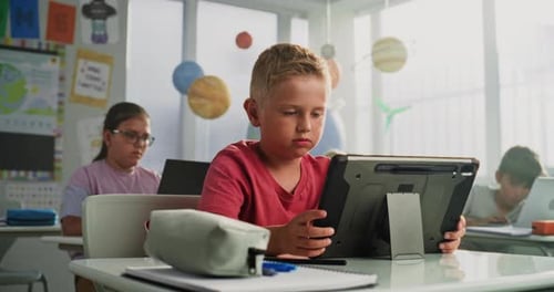 Computer Science Lesson Primary School Boy Sitting at Desk Using Tablet Computer in Classroom