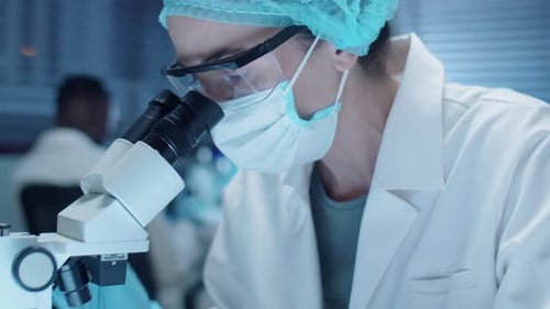Female Scientist in Mask Using Microscope in Laboratory