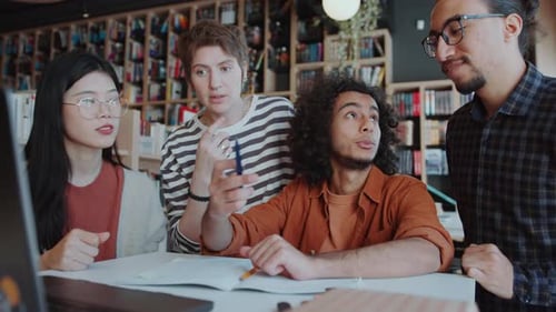 Group of Students Sharing Ideas about Project on Laptop in Library