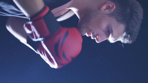 Vertical Video of Strong athlete punches punching bag in dusty gym.