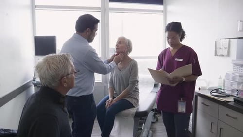 Doctor Examining Glands Of Senior Woman In Clinic Exam Room