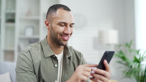 Young Adult Man Uses Smartphone at Home