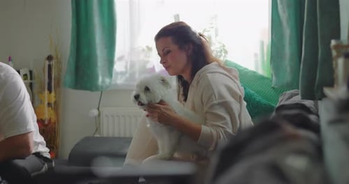 Woman Holds Small White Dog on Couch Indoors