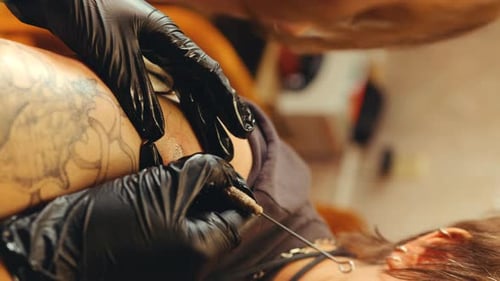 Mãos de tatuador em luvas injetando tinta na pele com agulha