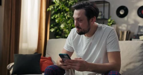 Man Sitting on Couch Using Smartphone in Living Room