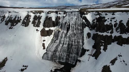 Majestic drone footage showcases breathtaking waterfall cascading down of spectacular snowcapped mou