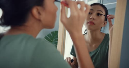 Asia lady with casual cloth put mascara on her eyelash in front of mirror in bedroom.