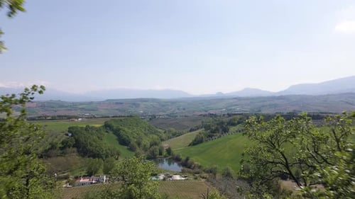 Drohnenaufnahme, die durch Bäume und Äste geht und eine weite, offene Szene eines Tals mit Ackerland zeigt, w