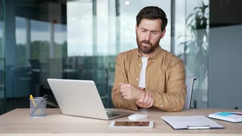 Man Rubbing Wrist at Modern Office Desk