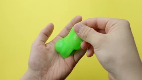 Person holding green slime in hands, yellow background