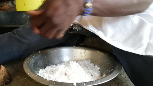 Person grating fresh coconut over bowl indoors