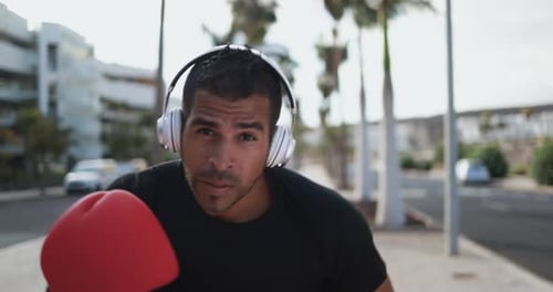 Man in Boxing Gloves Practicing Punches on Urban Sidewalk