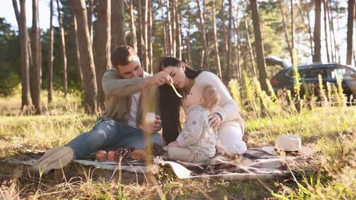 Feeding boy with child food. Family of father, mother and little son is outdoors in the forest