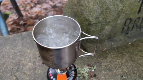Close up top view of a aluminum cup sitting on a small gas powered camping stove with boiling water